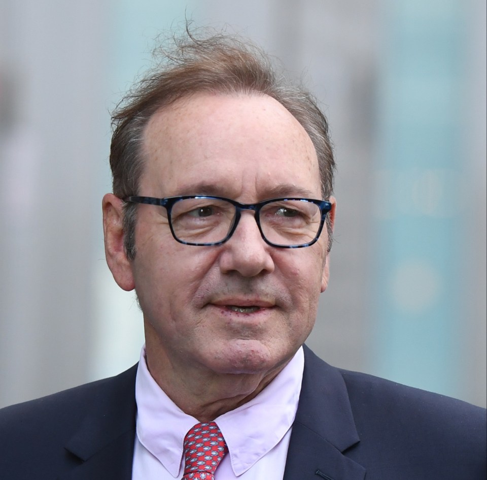 Kevin Spacey wearing a suit, pink shirt, and red patterned tie at Southwark Crown Court.