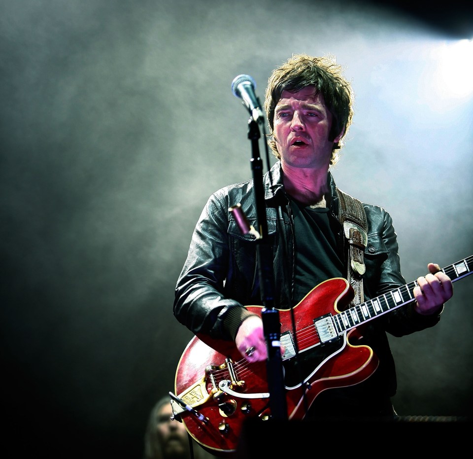 Noel Gallagher of Oasis performing on a red electric guitar.