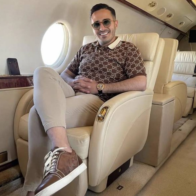 Simon Leviev, the Tinder Swindler, smiling in a private jet wearing a Gucci polo shirt.