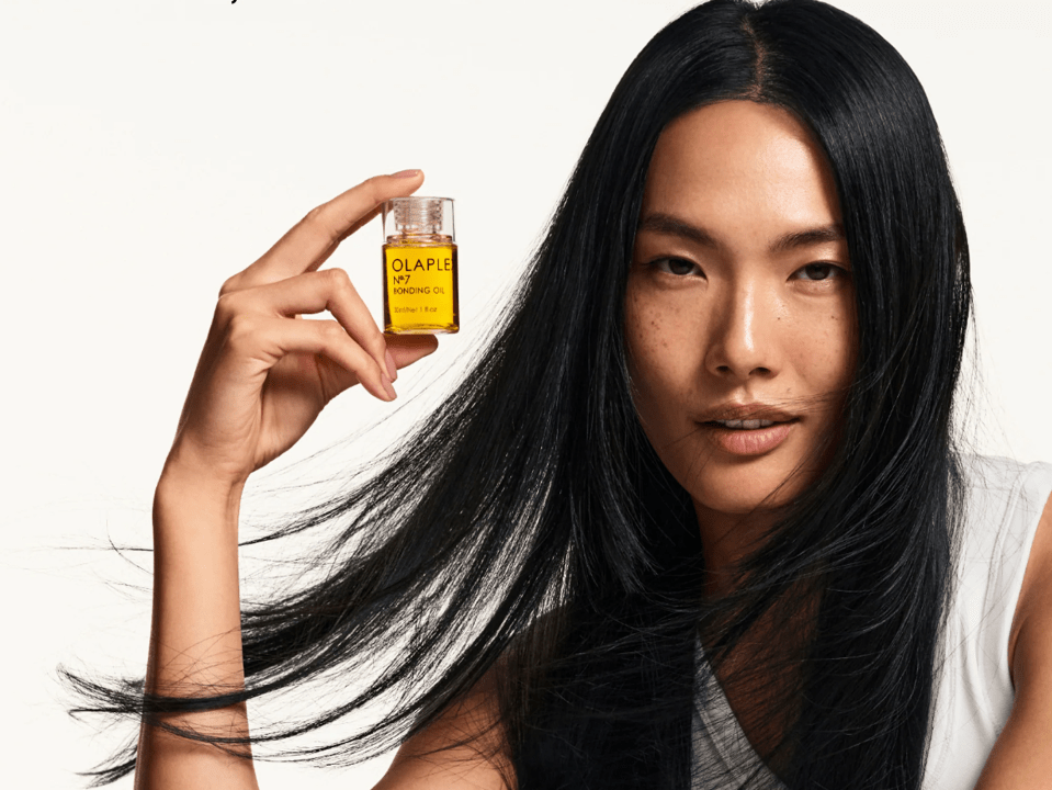 Woman with long black hair holding a bottle of Olaplex N°7 Bonding Oil.