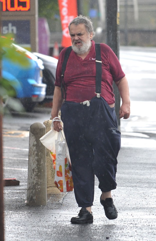 Brian Wilkinson walking in the rain with a shopping bag near a petrol station.