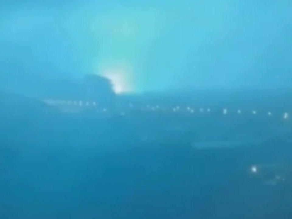 City skyline at night with a bright blue-green flash of light in the distance.