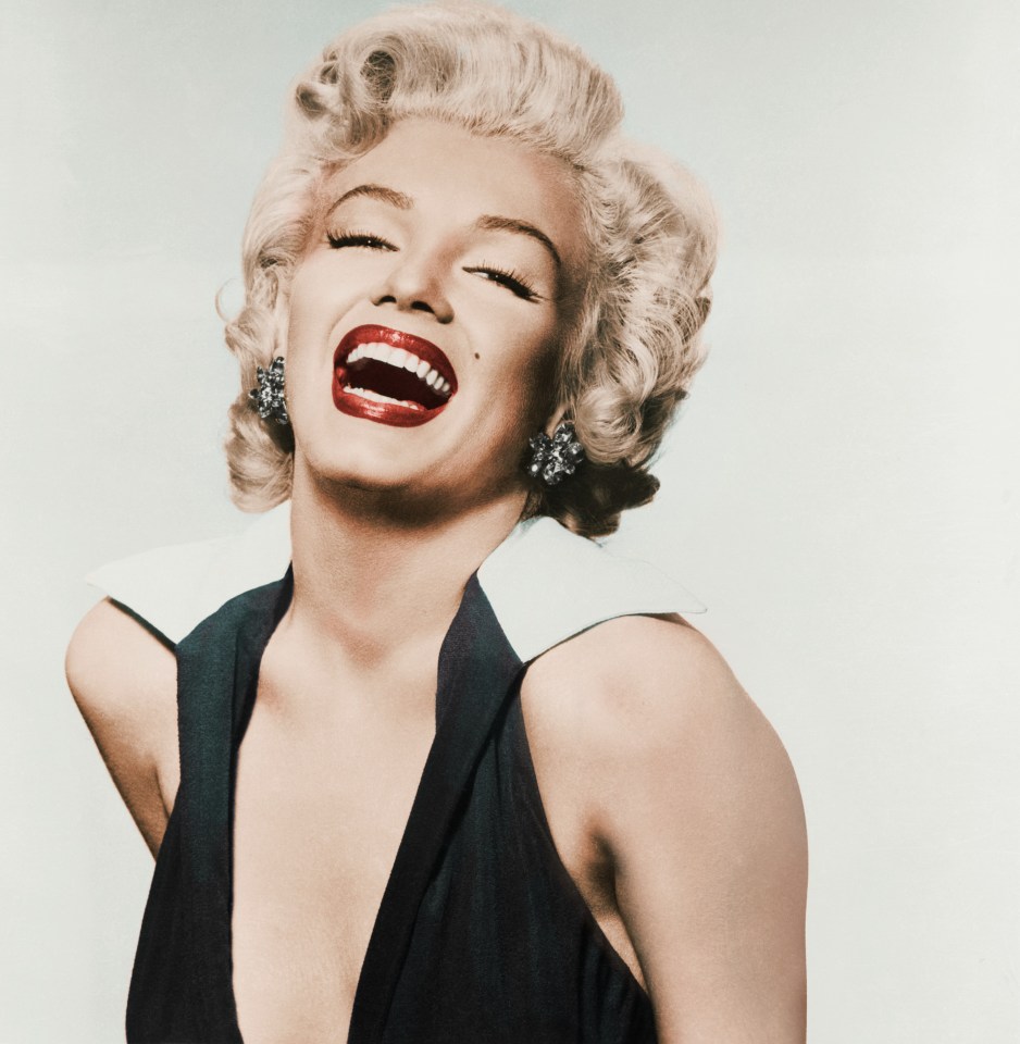 Marilyn Monroe laughing, wearing a black dress with a white collar and earrings.
