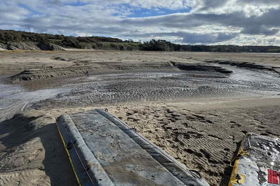 A man's chest, head, and one arm poking out from quicksand in Morecambe Bay as rescue crews save him from the rapidly approaching tide.