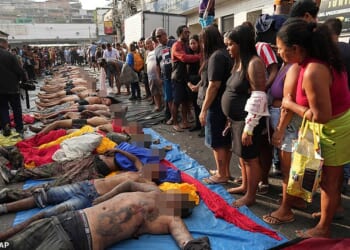 Rio de Janeiro's gang war has plunged into shocking brutality - with police accused of beheading a teenage gangster and hanging his head from a tree after Brazil 's bloodiest-ever favela raid. Pictured: Residents look at the bodies of people killed on Tuesday in Brazil