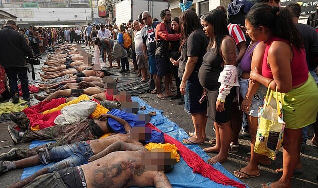 Rio de Janeiro's gang war has plunged into shocking brutality - with police accused of beheading a teenage gangster and hanging his head from a tree after Brazil 's bloodiest-ever favela raid. Pictured: Residents look at the bodies of people killed on Tuesday in Brazil