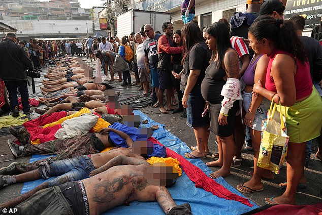 Rio de Janeiro's gang war has plunged into shocking brutality - with police accused of beheading a teenage gangster and hanging his head from a tree after Brazil 's bloodiest-ever favela raid. Pictured: Residents look at the bodies of people killed on Tuesday in Brazil