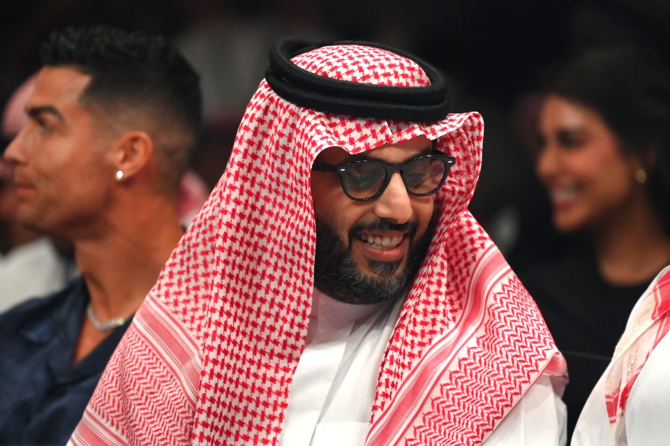 Turki Al-Sheikh smiling while sitting ringside at a boxing match.