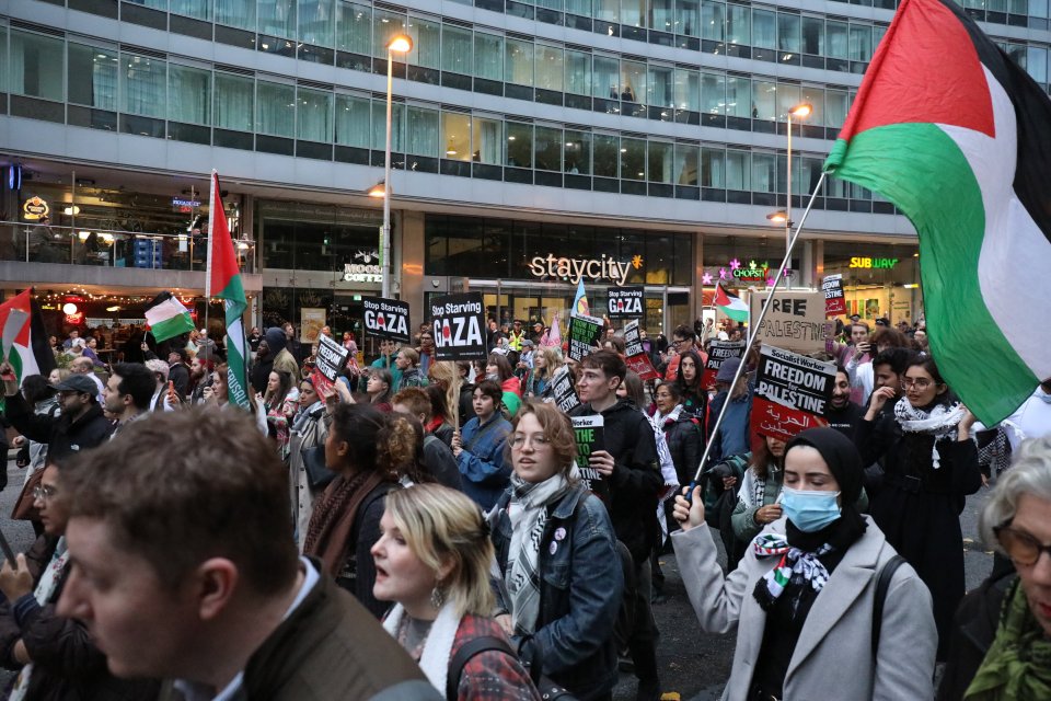Pro-Palestinian protestors marching in Manchester, holding signs such as "Stop Starving Gaza" and "Freedom for Palestine," with several Palestinian flags visible.