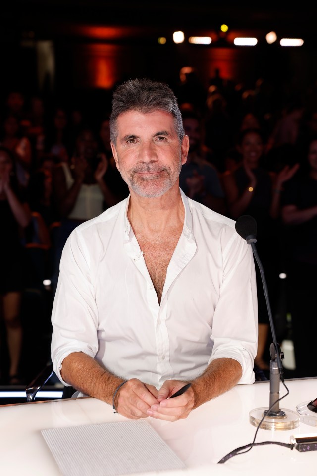 Simon Cowell, judge on America's Got Talent, sitting at a desk with a microphone.