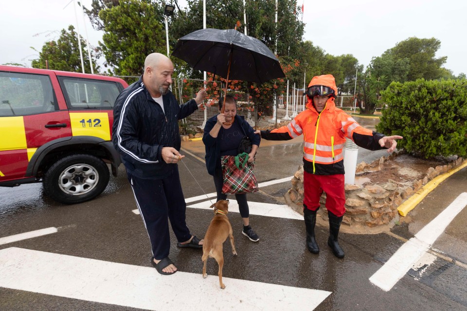 A firefighter evacuates residents and a dog from a campsite during heavy rain.