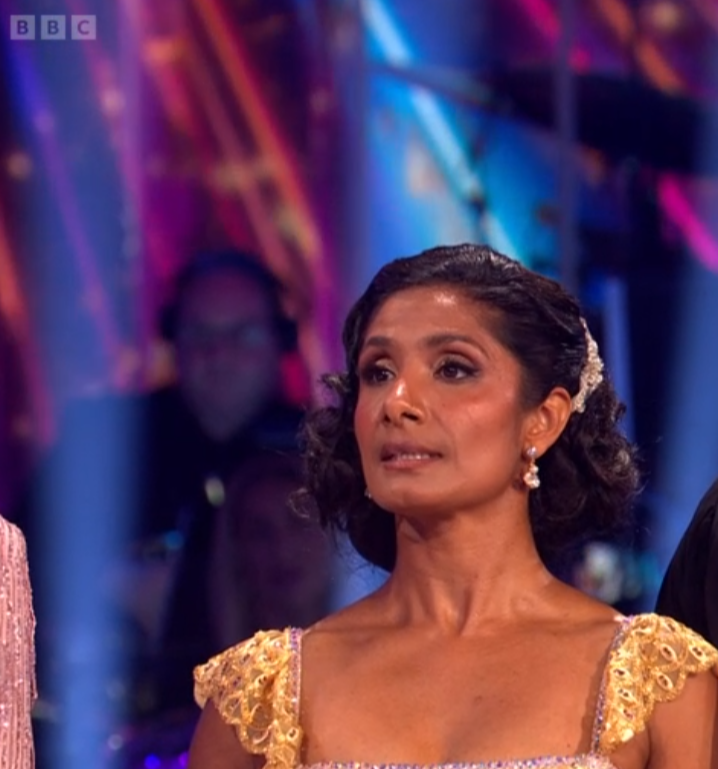 Woman with dark hair and a gold dress looks toward her right.