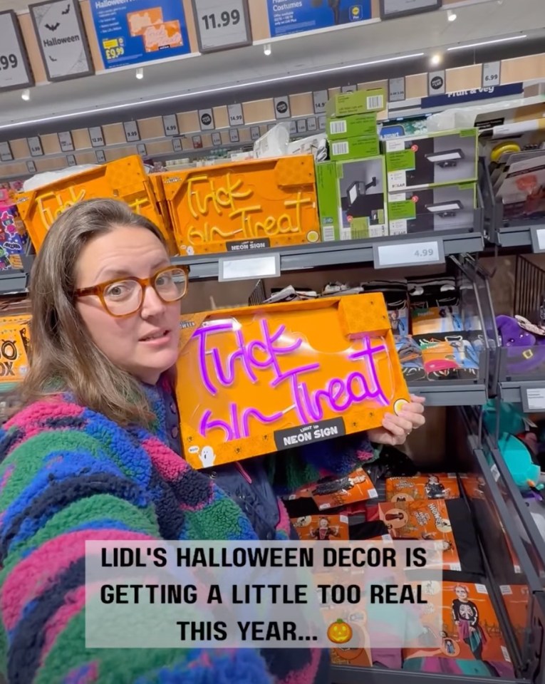 A person holding a "Trick or Treat" neon sign in a store aisle.