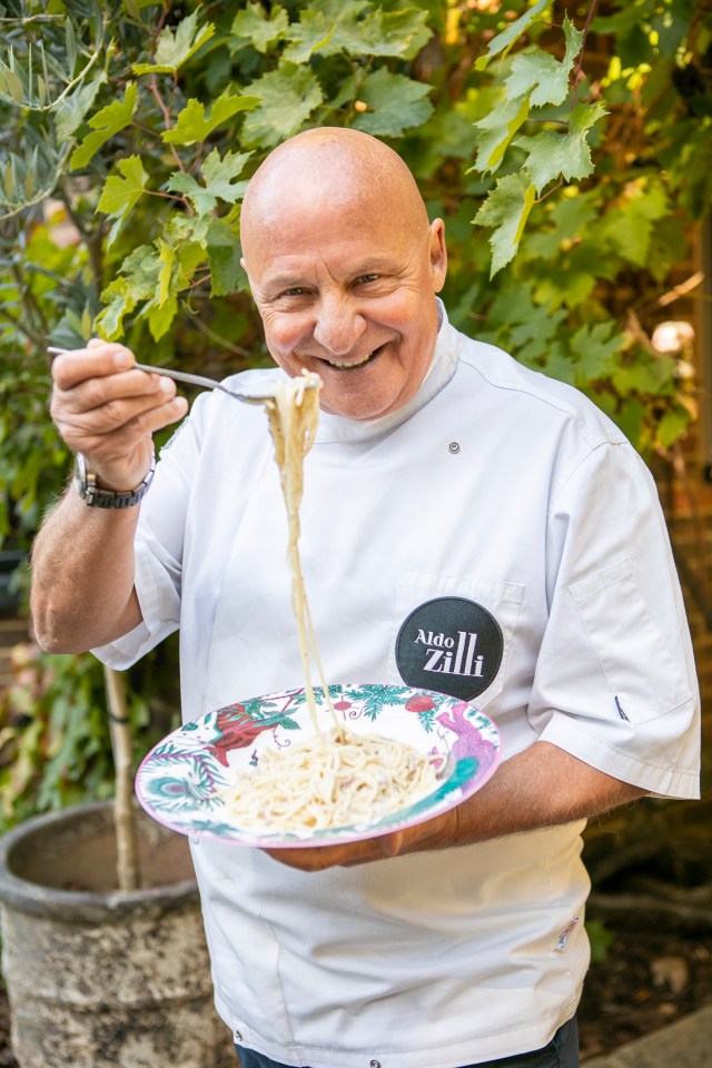 Aldo Zilli holding a plate of supermarket carbonara, with spaghetti wrapped around a fork.