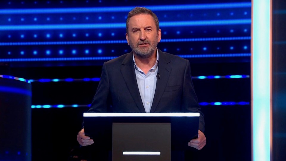 Lee Mack hosts "The 1% Club" against a backdrop of blue lights.