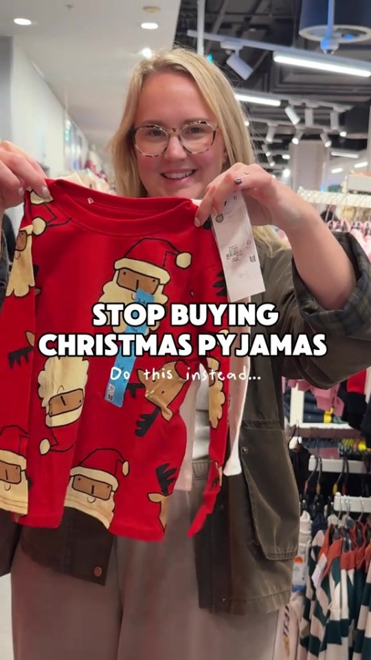 A woman in glasses holding up red Christmas pajamas with Santa and reindeer designs.