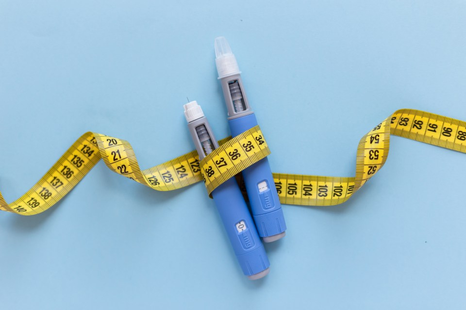 Two blue injection pens, for antidiabetic or anti-obesity medication, wrapped with a yellow measuring tape on a light blue background.