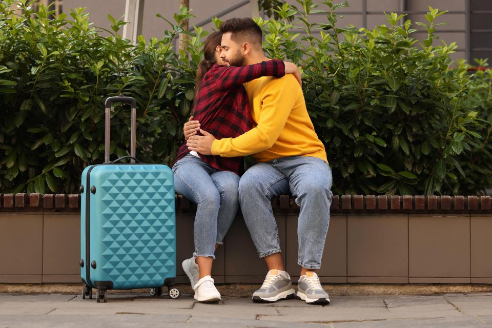 Couple hugging on a bench with a turquoise suitcase beside them.