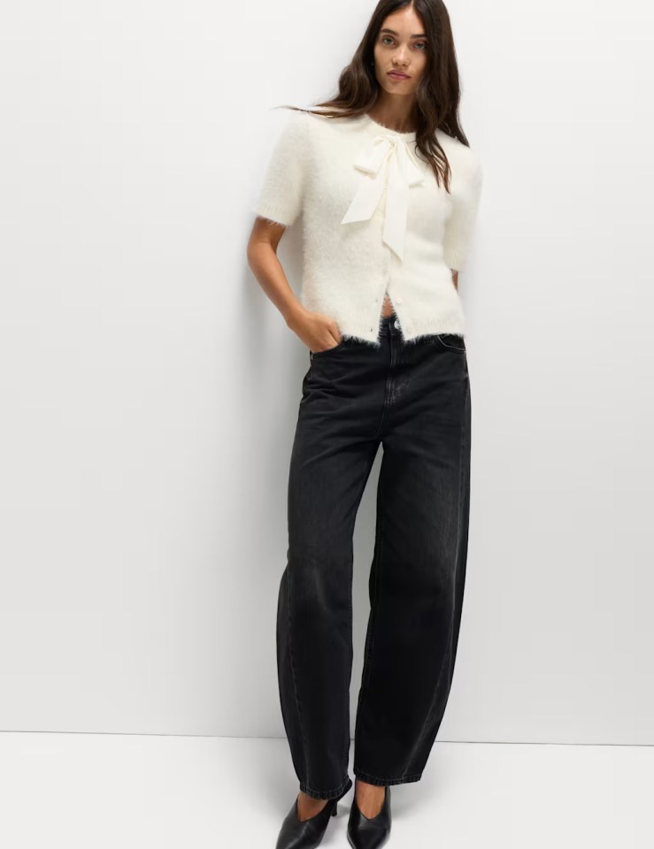 Woman wearing a cream fuzzy crew neck bow cardigan and black wide-leg jeans.