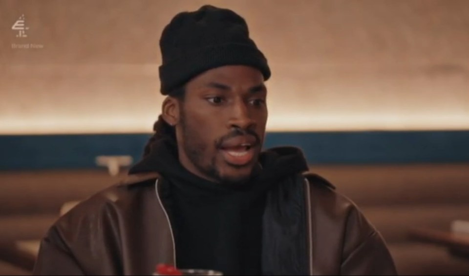 A man in a black beanie and brown jacket talking.