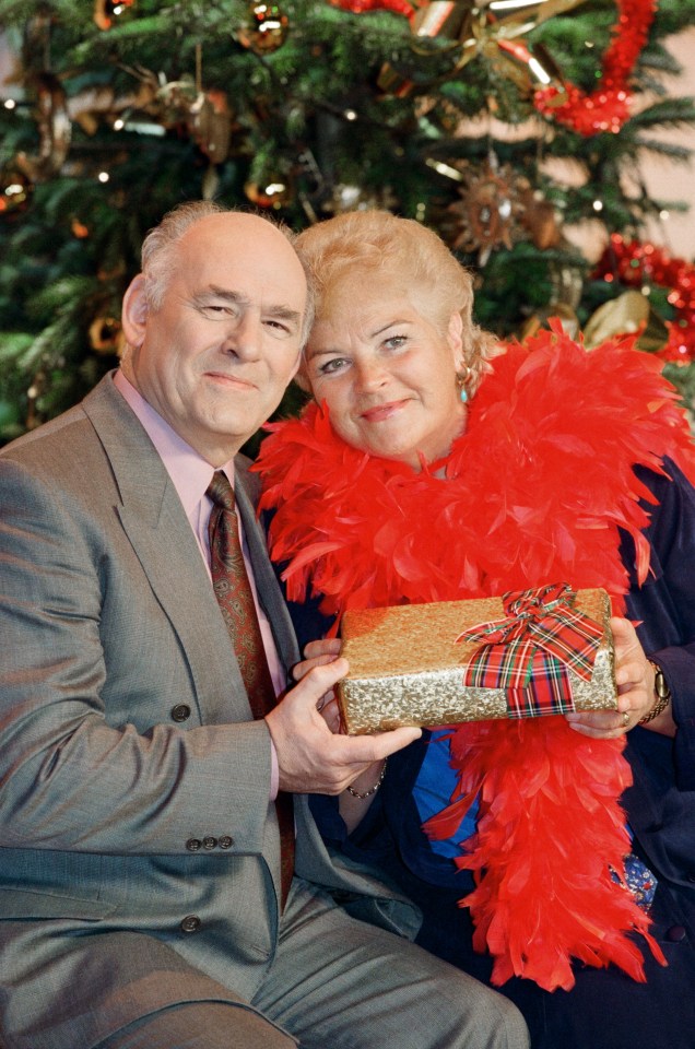 EastEnders actors Tony Caunter and Pam St. Clement holding a Christmas gift.