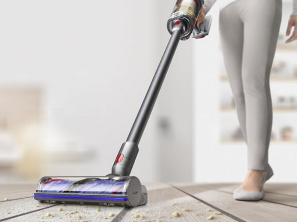 A person vacuums a dusty wooden floor with a stick vacuum.