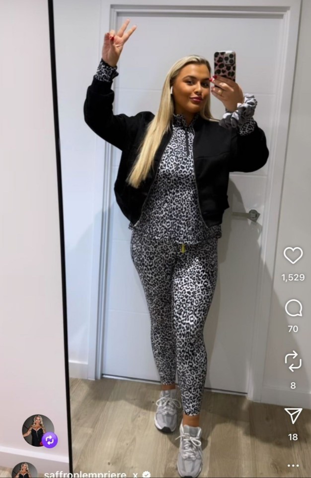 Saffron Lempriere taking a mirror selfie, showing off her figure in a leopard print tracksuit and black jacket, with her blonde hair down and making a peace sign.
