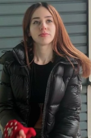 A young woman, Emily Whittaker, with long auburn hair wearing a black puffer jacket.