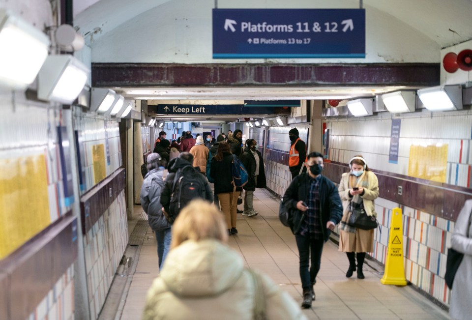 Commuters in face masks walk through a tunnel in London's Clapham Junction station.