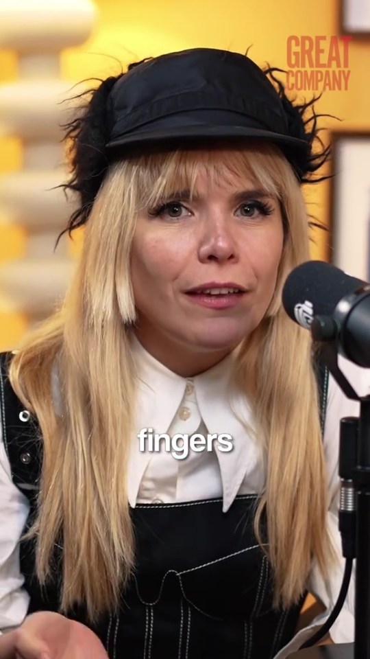 Paloma Faith wearing a black cap and white shirt, speaking into a microphone.