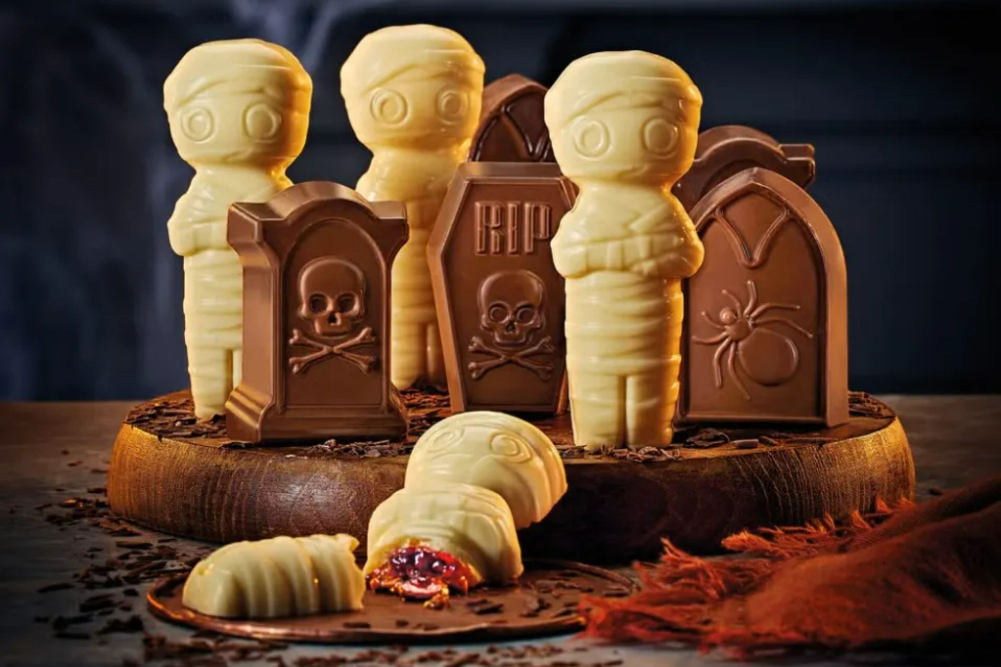 An image collage containing 1 images, Image 1 shows White chocolate mummies and milk chocolate tombstones on a wooden stand