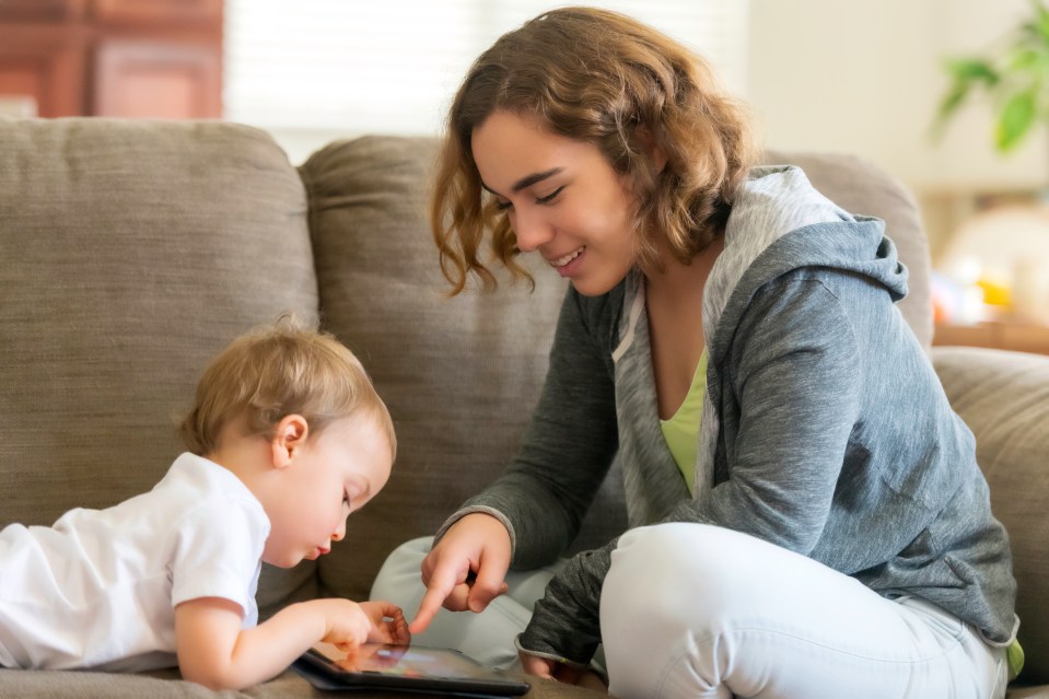 Smiling young woman and child interacting with a digital tablet on a couch.