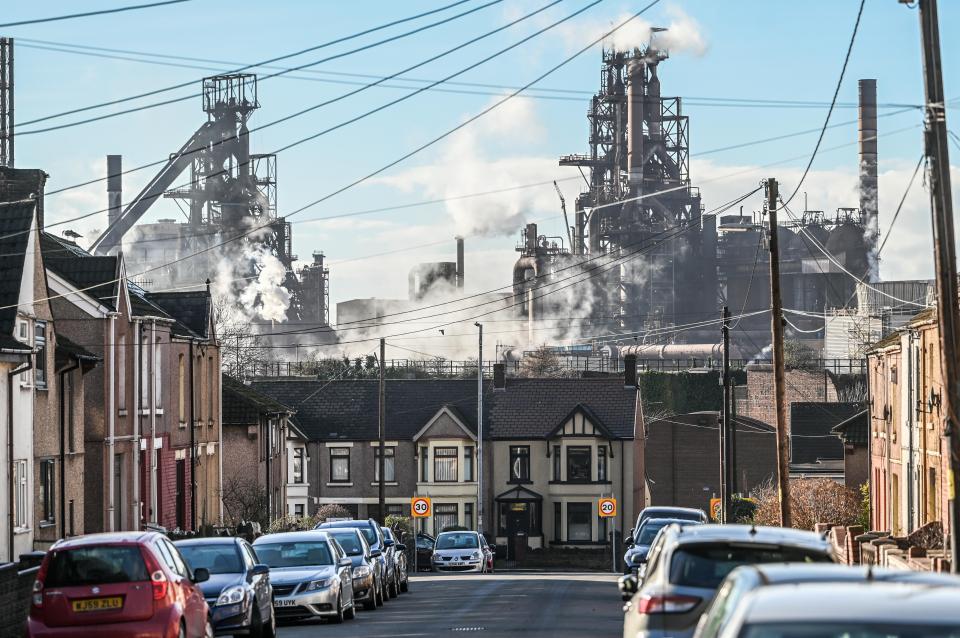 The Port Talbot Tata Steel blast furnaces emitting smoke and steam, towering over residential homes and parked cars in Wales.