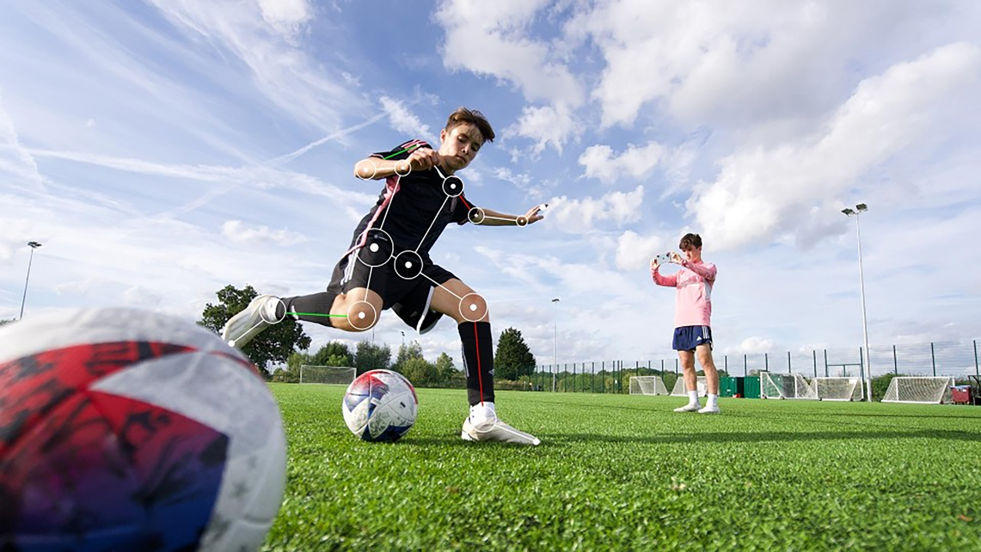 A soccer player with motion tracking lines on his body is being filmed by another player with a phone.
