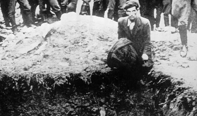 The heartbreaking photograph shows a German soldier aiming a gun at a man kneeling beside a mass grave while he looks into the distance