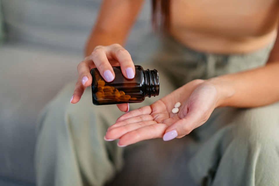 A woman pouring two pills from a brown bottle into her palm.