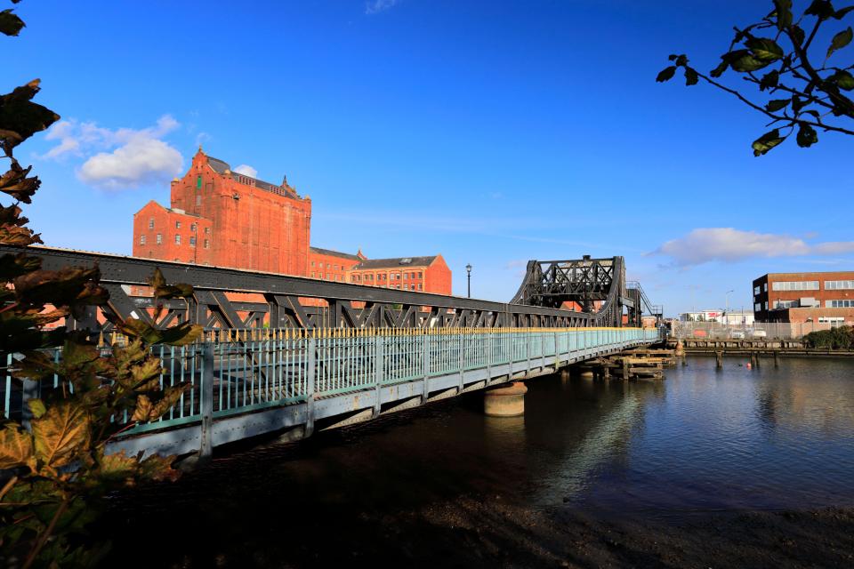 The Corporation Bridge, a Scherzer rolling lift bascule bridge, crosses the Old Dock in Grimsby, with red brick buildings in the background.