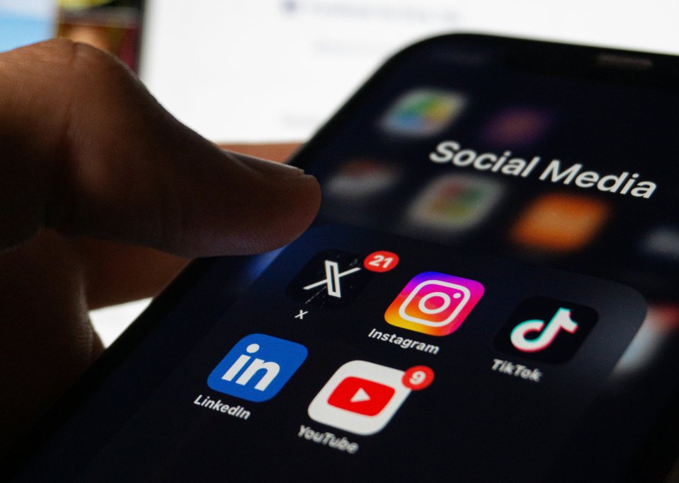 Hand holding a phone with social media apps on its screen including LinkedIn, YouTube, Instagram, X, and TikTok.