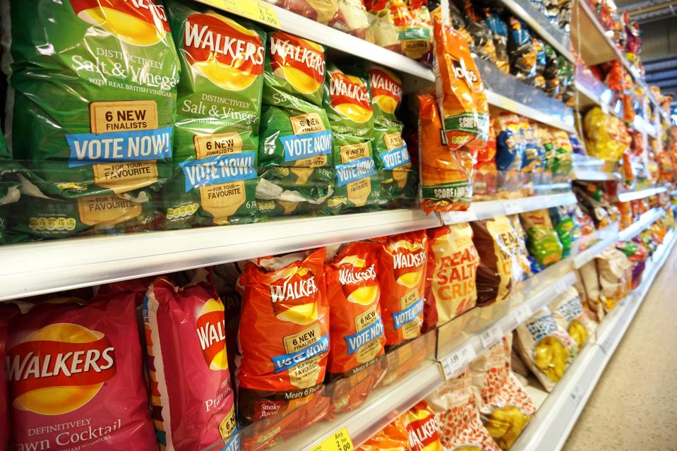 Crisps and snacks from Walkers and Tesco on shelves in a UK supermarket.