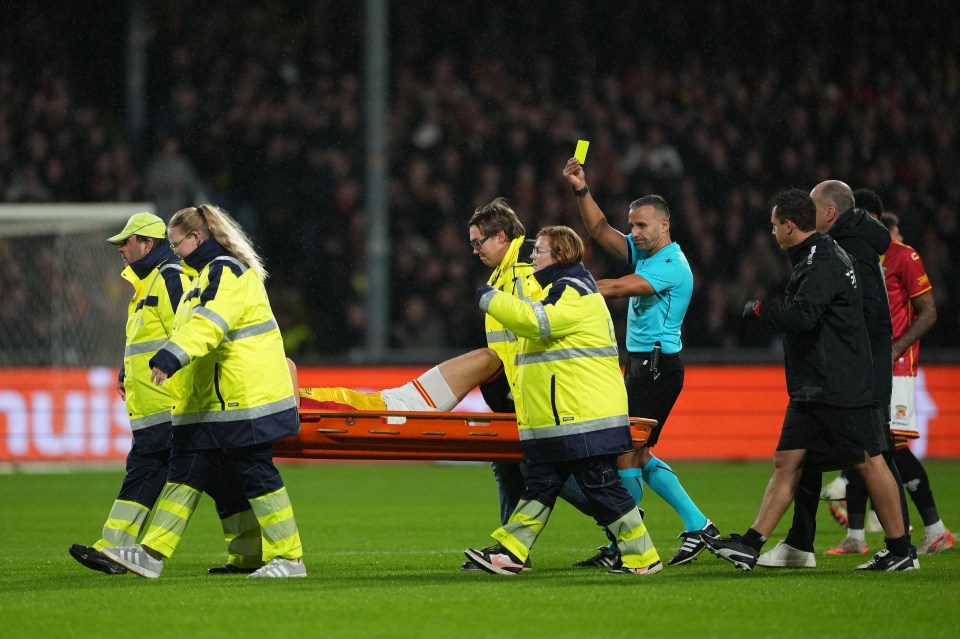 A soccer referee gives a yellow card as paramedics carry an injured player off the field on a stretcher during the Go Ahead Eagles v Aston Villa FC UEFA Europa League 2025/26 League Phase MD3 match.