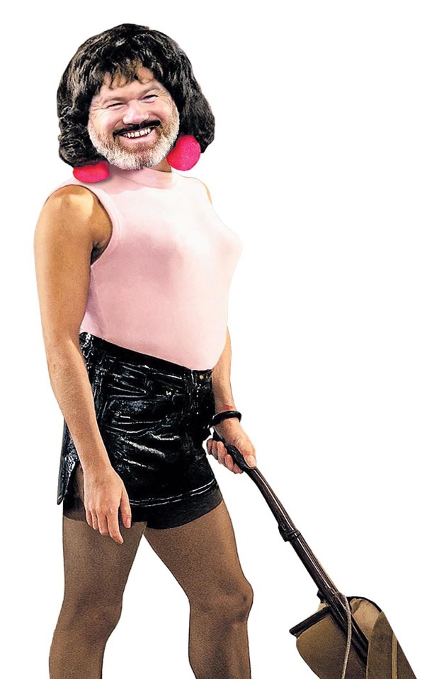 A person with a beard and dark wig, wearing a pink top, black shorts, and tights, holds a vacuum cleaner.