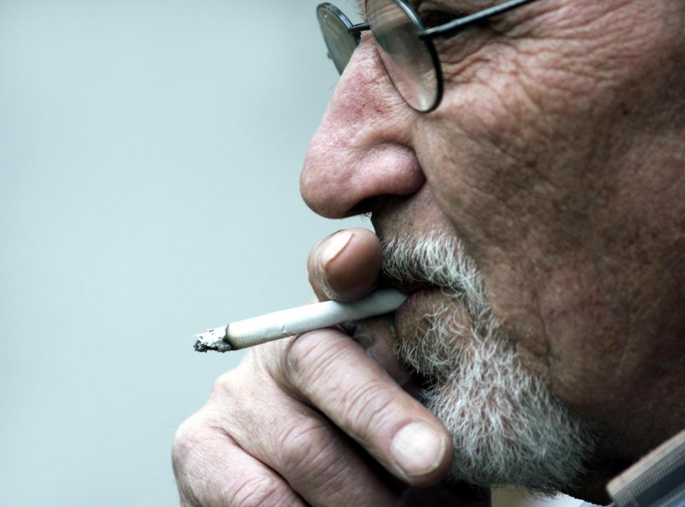 Close-up of an elderly man with glasses smoking a cigarette.