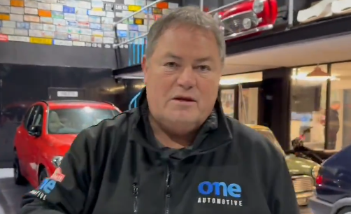 Mike Brewer, host of Wheeler Dealers, wearing a black zip-up jacket with "one AUTOMOTIVE" written on it.