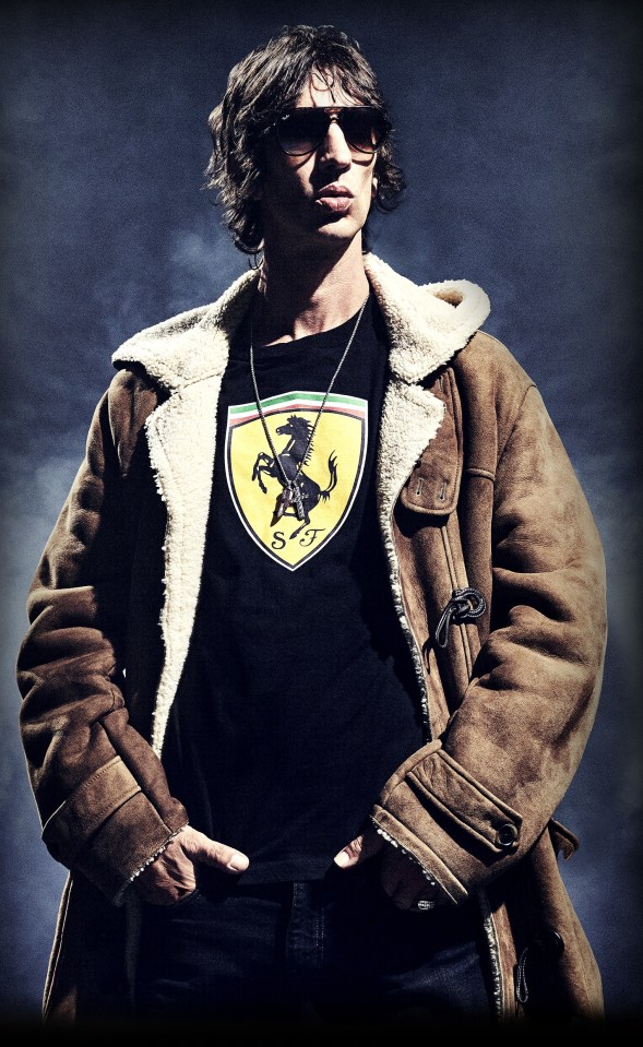 Richard Ashcroft wearing sunglasses, a brown shearling coat, and a black Ferrari t-shirt.