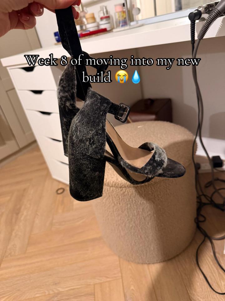 A woman holds up a pair of black velvet heels covered in mold, with the text "Week 8 of moving into my new build" and crying emojis.