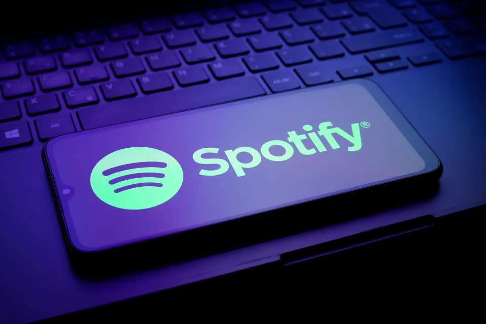 A phone screen displays the Spotify logo and name on a keyboard.