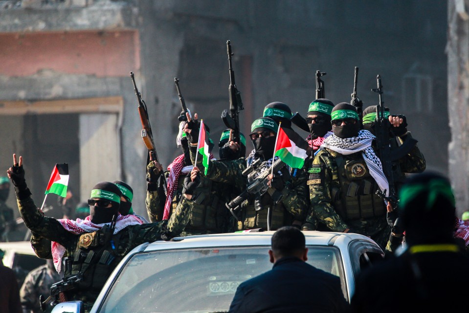 Hamas militants on a car in Jabalia ahead of a hostage exchange, displaying weapons and Palestinian flags.