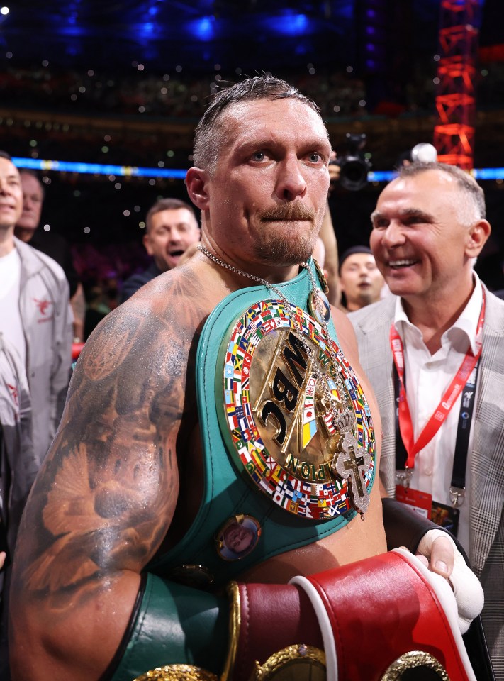 Oleksandr Usyk wearing multiple championship belts after a boxing match.