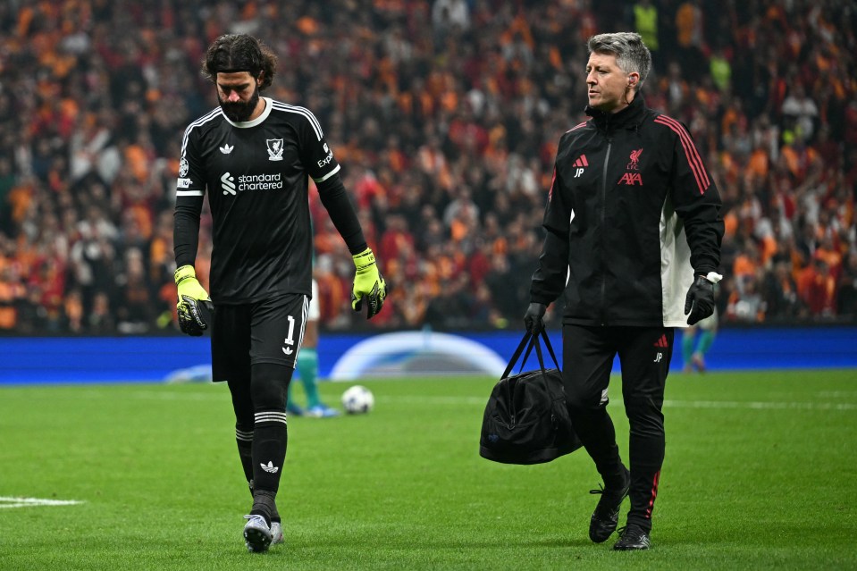 Liverpool goalkeeper Alisson walks off the pitch with a medical staff member.