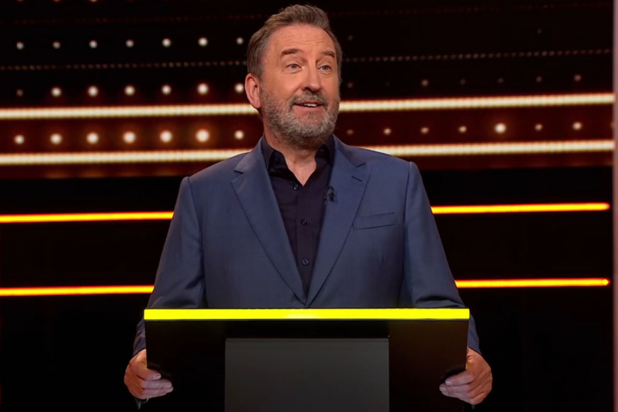 An image collage containing 1 images, Image 1 shows Lee Mack standing at a podium on The 1% Club set